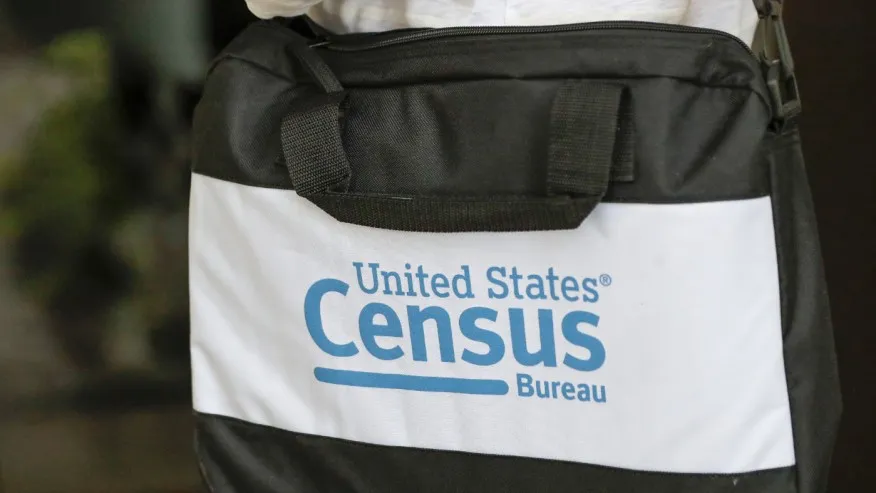 A census taker’s briefcase is visible as she knocks on doors