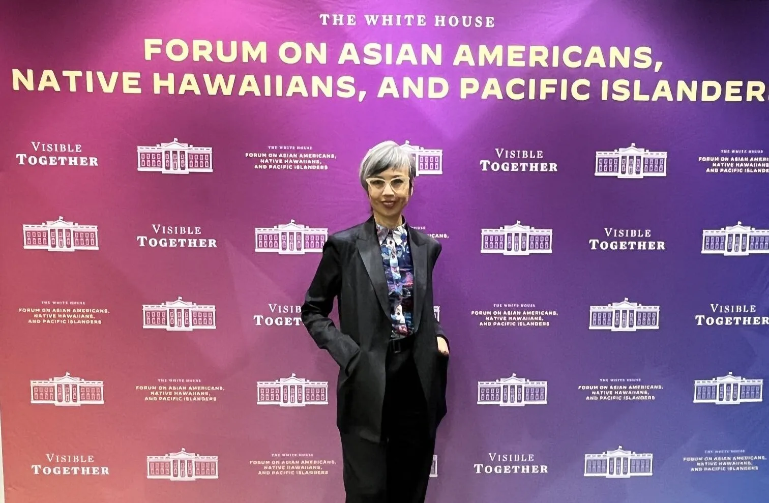 Ninez Ponce standing in front of a banner that says The White House Forum on Asian Americans, Native Hawaiians, and Pacific Islanders