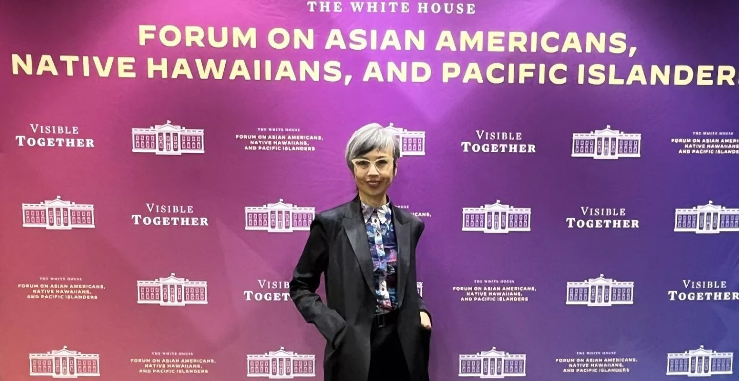 Ninez Ponce standing in front of a banner that says The White House Forum on Asian Americans, Native Hawaiians, and Pacific Islanders