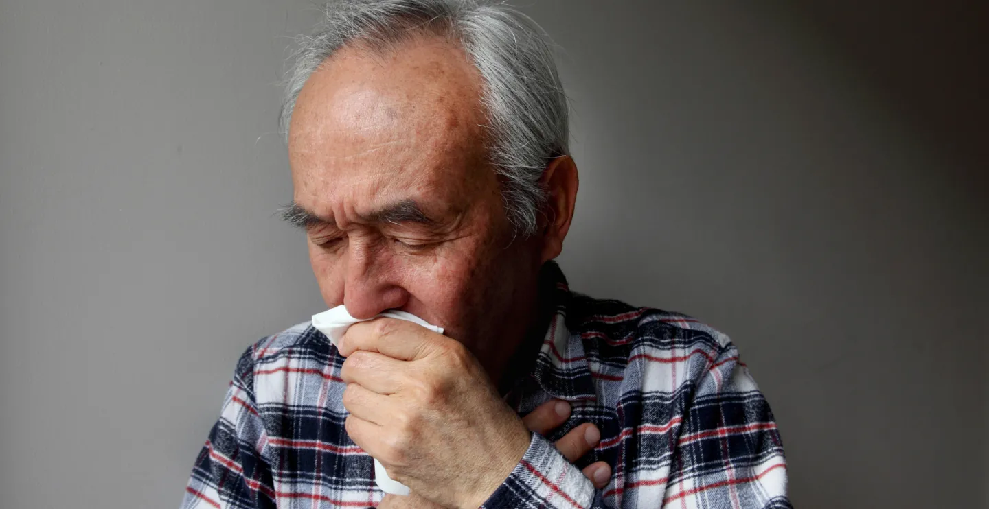 older man coughing into a napkin