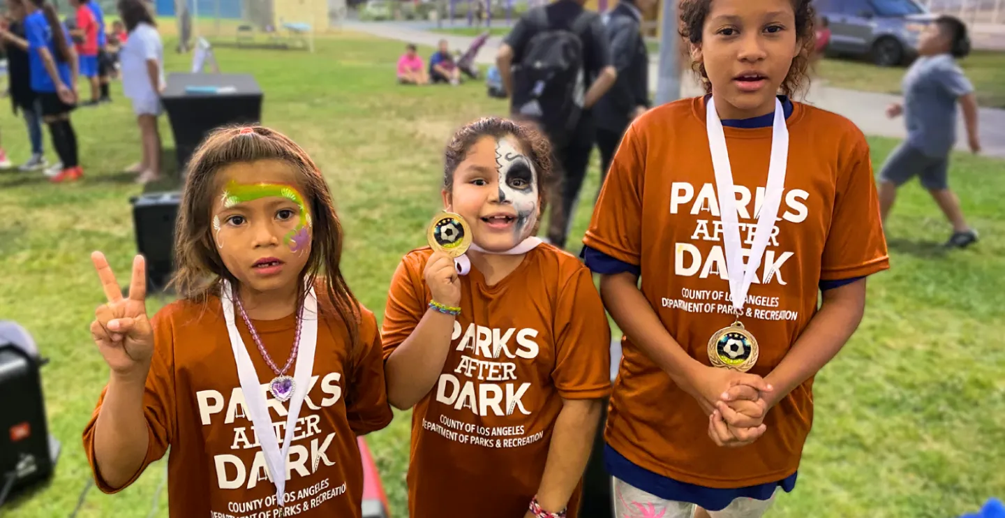 Three children wearing brown T-shirts that read Parks After Dark