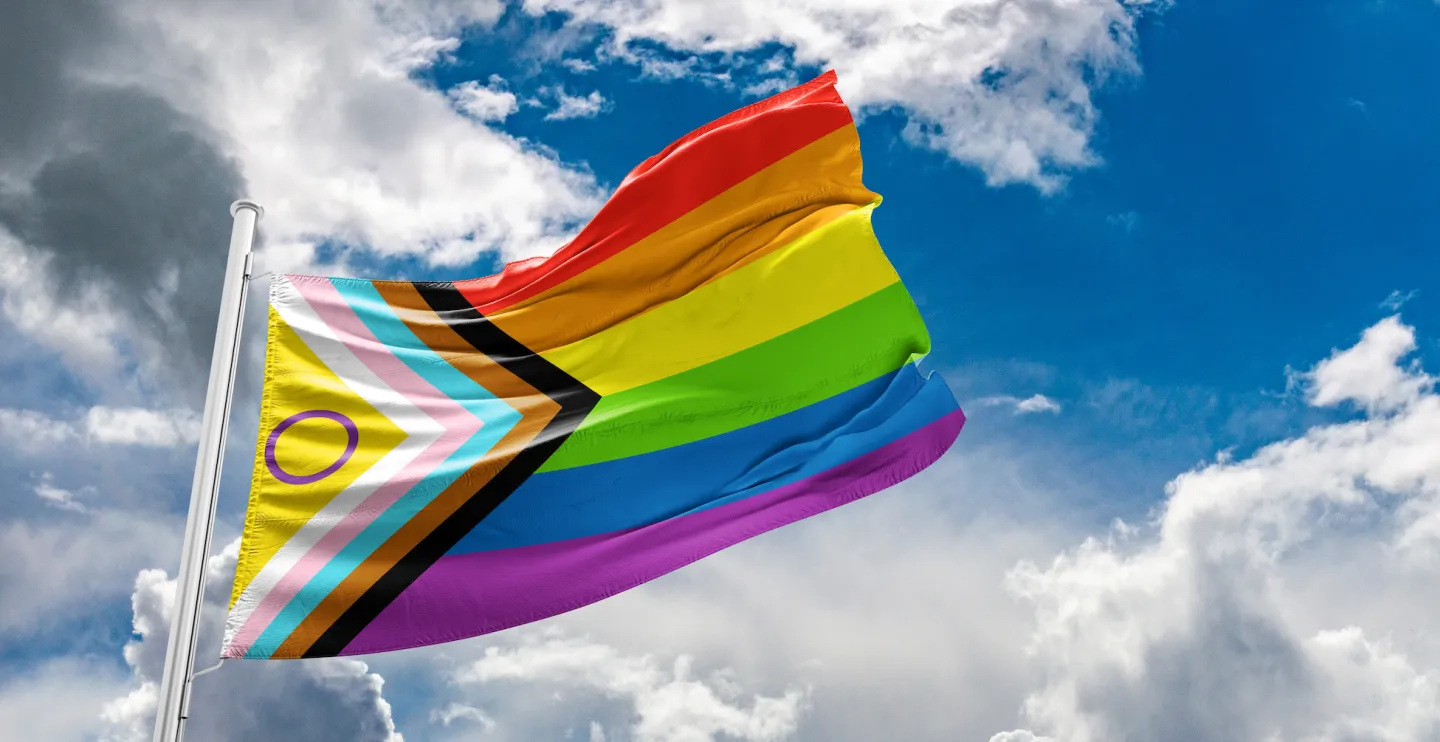 LGBTQ progress flag flying with the sky and clouds in the background