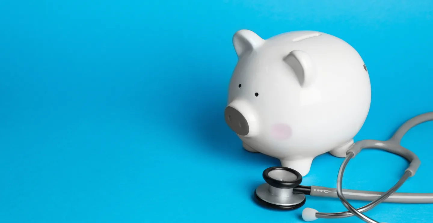 White ceramic piggy bank and stethoscope on light blue background