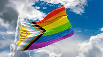 LGBTQ progress flag flying with the sky and clouds in the background