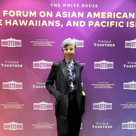 Ninez Ponce standing in front of a banner that says The White House Forum on Asian Americans, Native Hawaiians, and Pacific Islanders