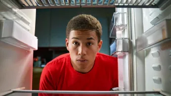 A young Black adult looks into an empty refrigerator